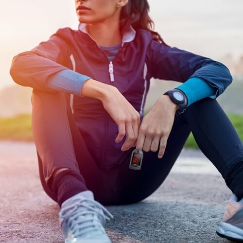 Woman in athletic wear sitting on the ground with a wearable device.